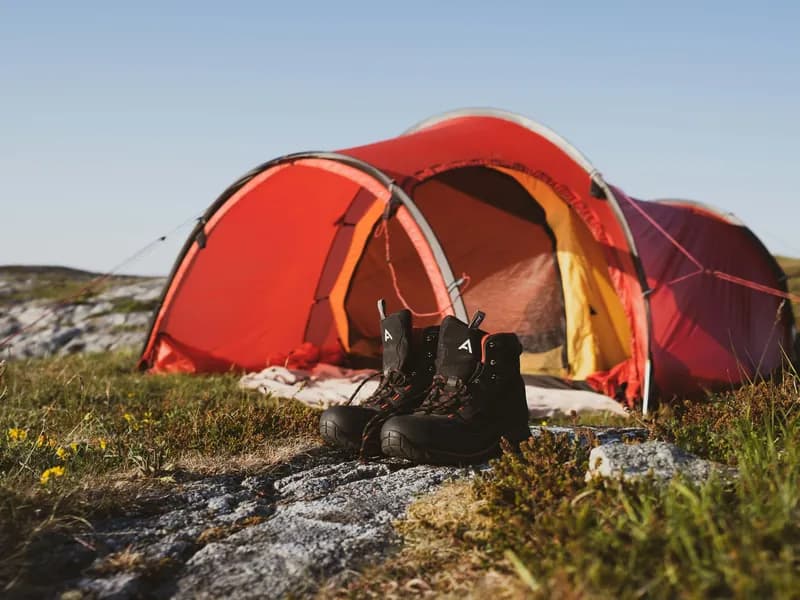 Telt og tursekk ved en fjord med fjell i bakgrunnen
