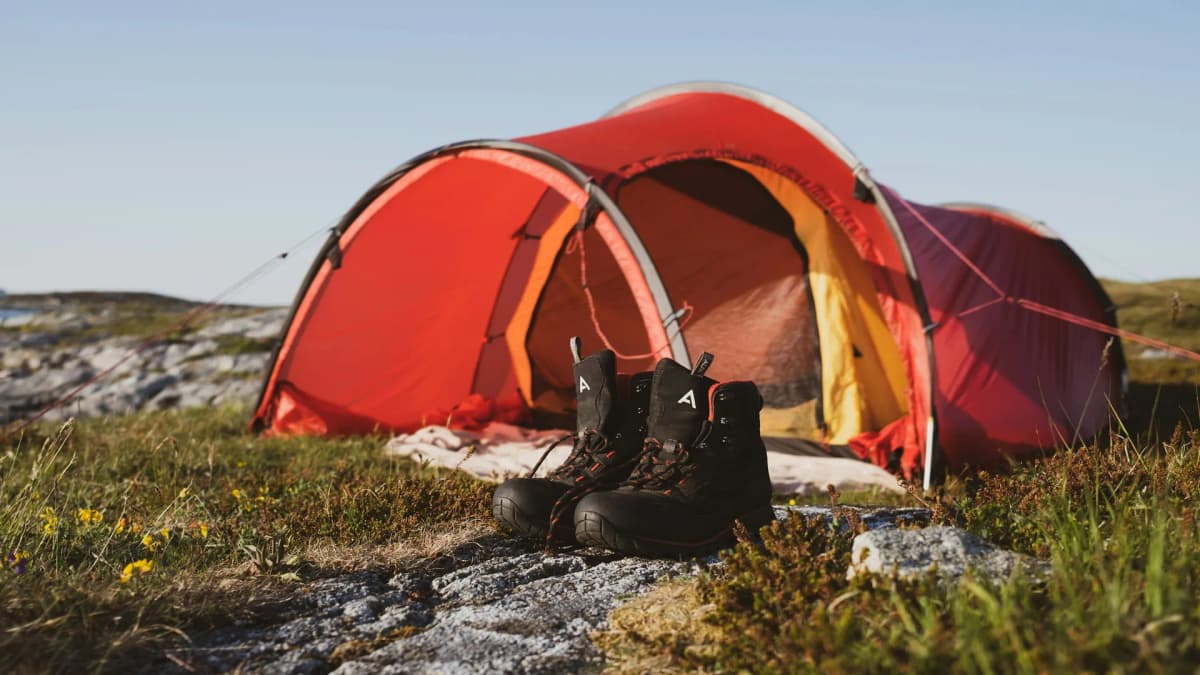 Telt og tursekk ved en fjord med fjell i bakgrunnen